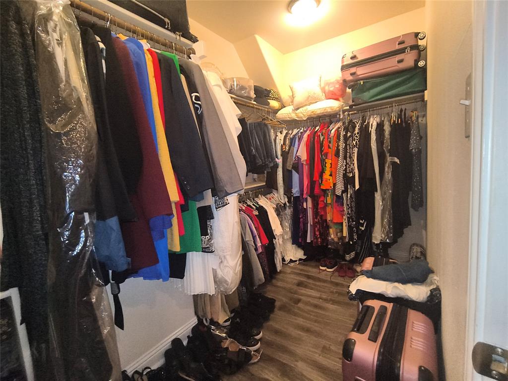 Walk-in closet with wood-finish flooring, ample hanging rods, and integrated shelving