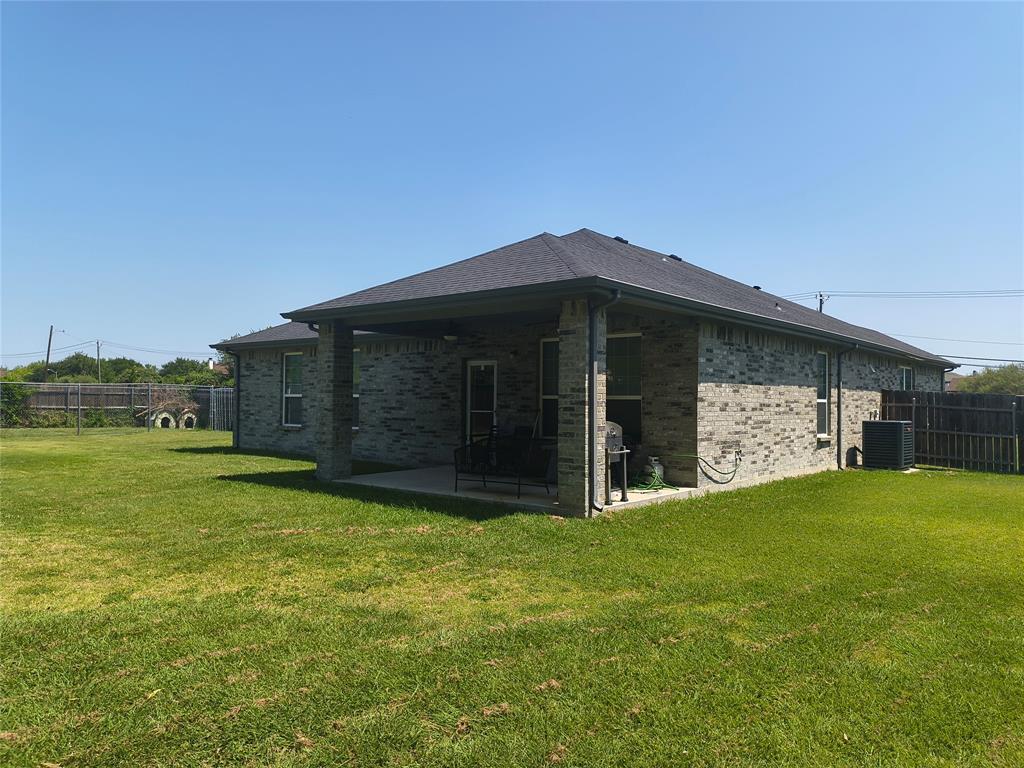 Spacious backyard featuring a covered patio, brick exterior, dark shingle roof, and a wood privacy fence