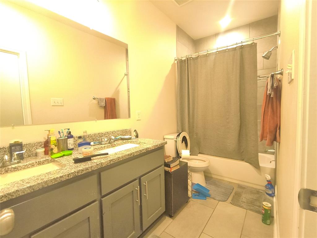 Bathroom featuring a dual-sink vanity with a granite-style countertop, gray cabinetry, a tub/shower combination with subway tile surround, and light-toned floor tile