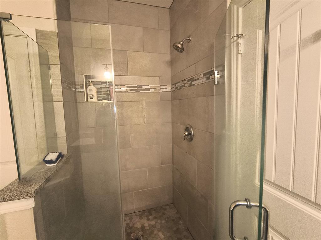Shower enclosure with clear glass panels, subway-style wall tiling, mosaic accent band, built-in recessed shelf, and hexagonal floor tiling