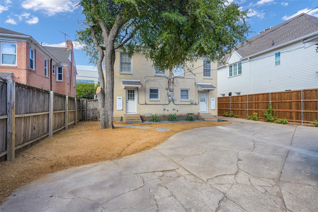 Two-story light brick exterior with a concrete parking area and wood-style privacy fencing