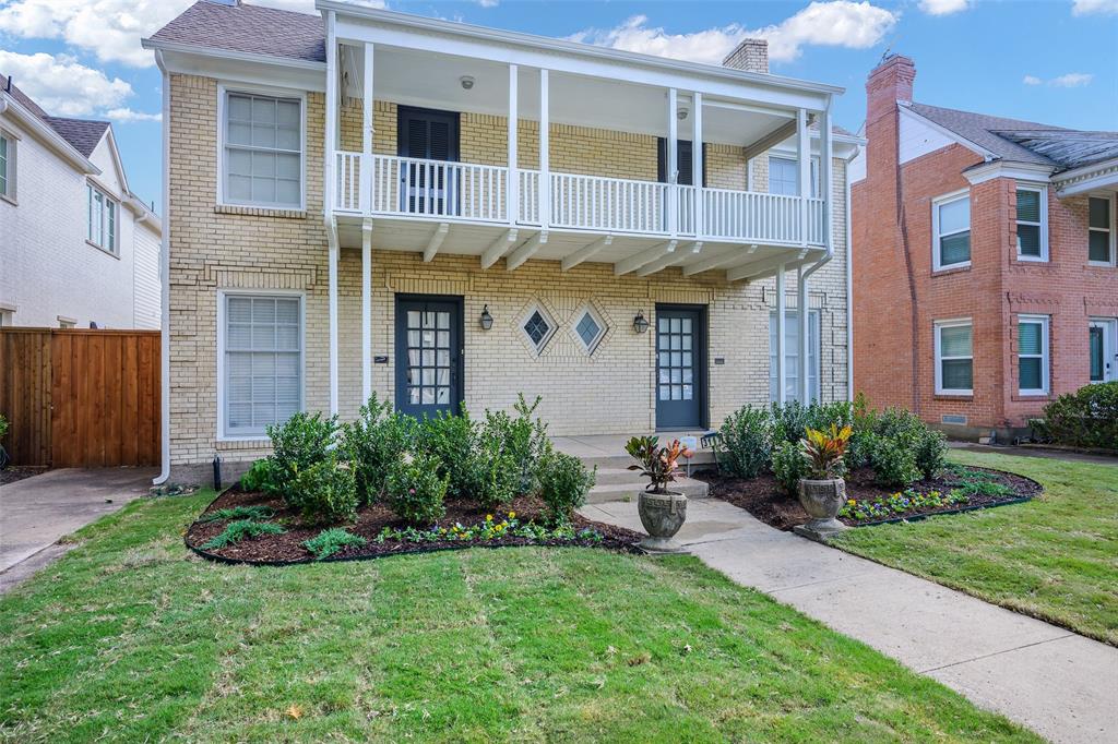 Two-story brick exterior featuring a full-width upper-level covered balcony, dual entryways with grid-paneled doors, decorative diamond-shaped windows, and a concrete walkway