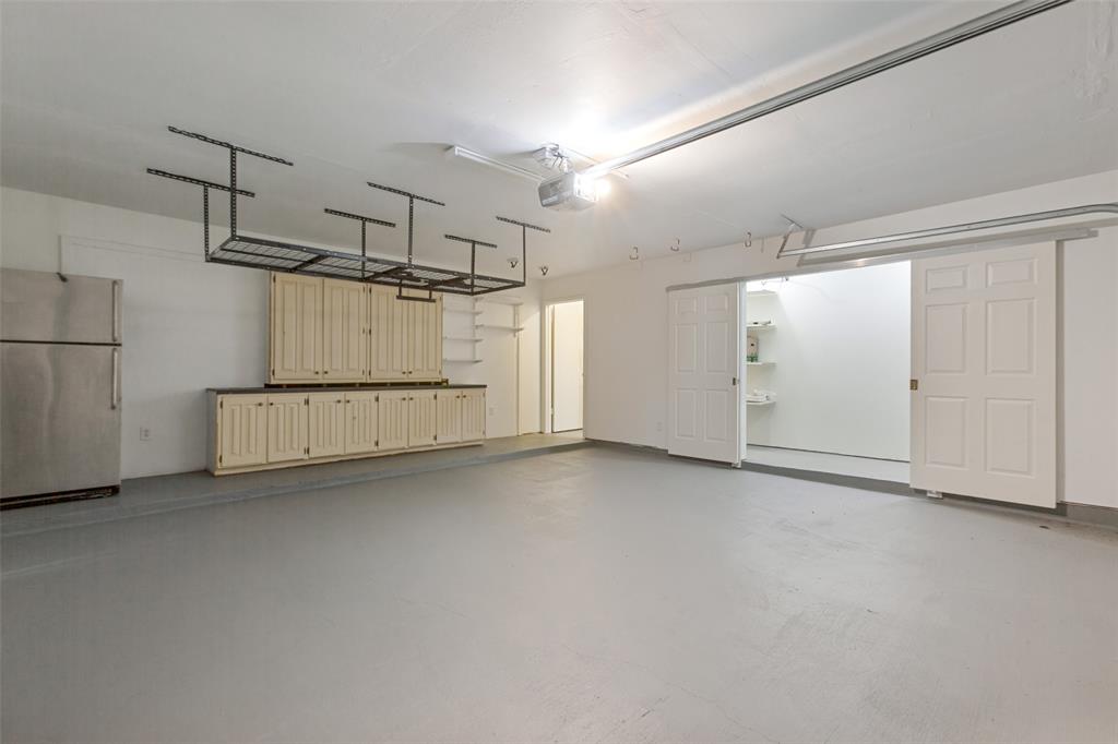 Spacious garage featuring freshly painted flooring, custom wood-finish cabinetry with ample storage, integrated ceiling-mounted organization system, and recessed lighting throughout