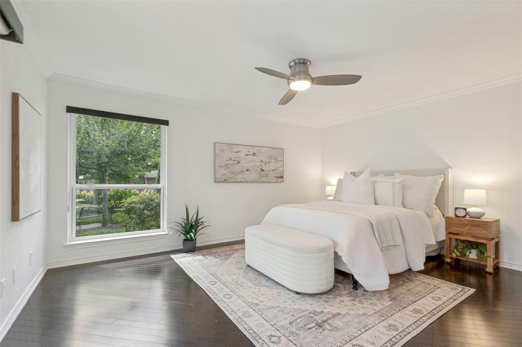 Dark wood-finish flooring, white walls, large window with roller shade, ceiling fan with integrated lighting, and crown molding