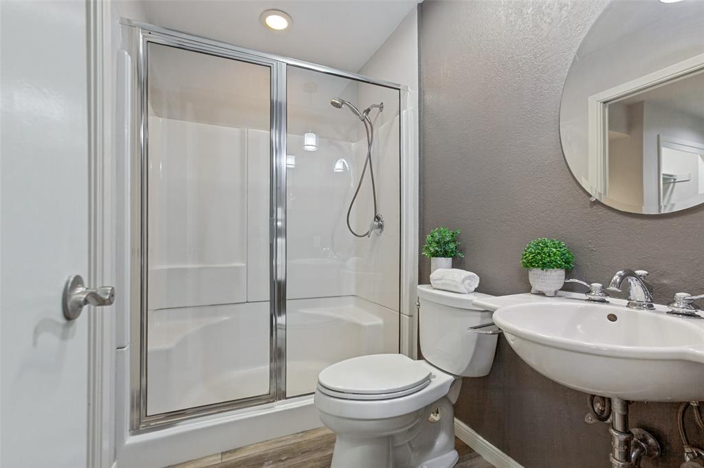Glass-enclosed shower with white surround, recessed lighting, wall-mounted sink with chrome faucet, and wood-finish flooring