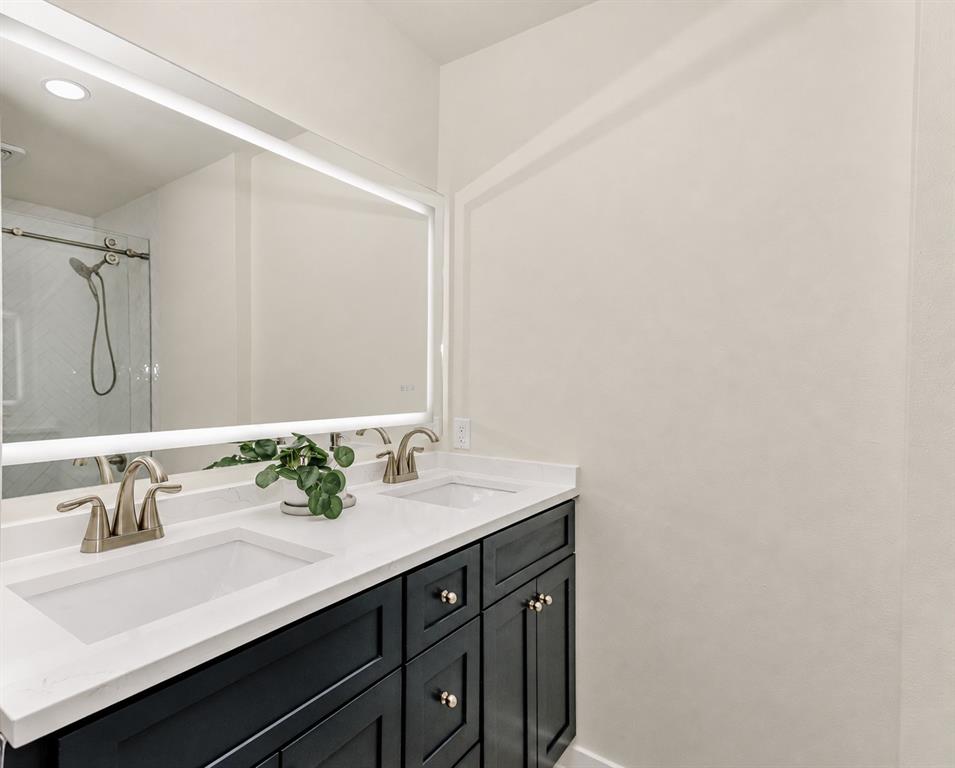 Ensuite Bath for the 2nd Bedroom. Dual vanity with integrated sinks, white countertops, dark wood-finish cabinetry, and an illuminated mirror