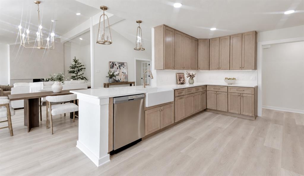 Wide Open-concept kitchen featuring light wood-finish flooring, white quartz countertops, a large farmhouse sink, and stainless steel appliances