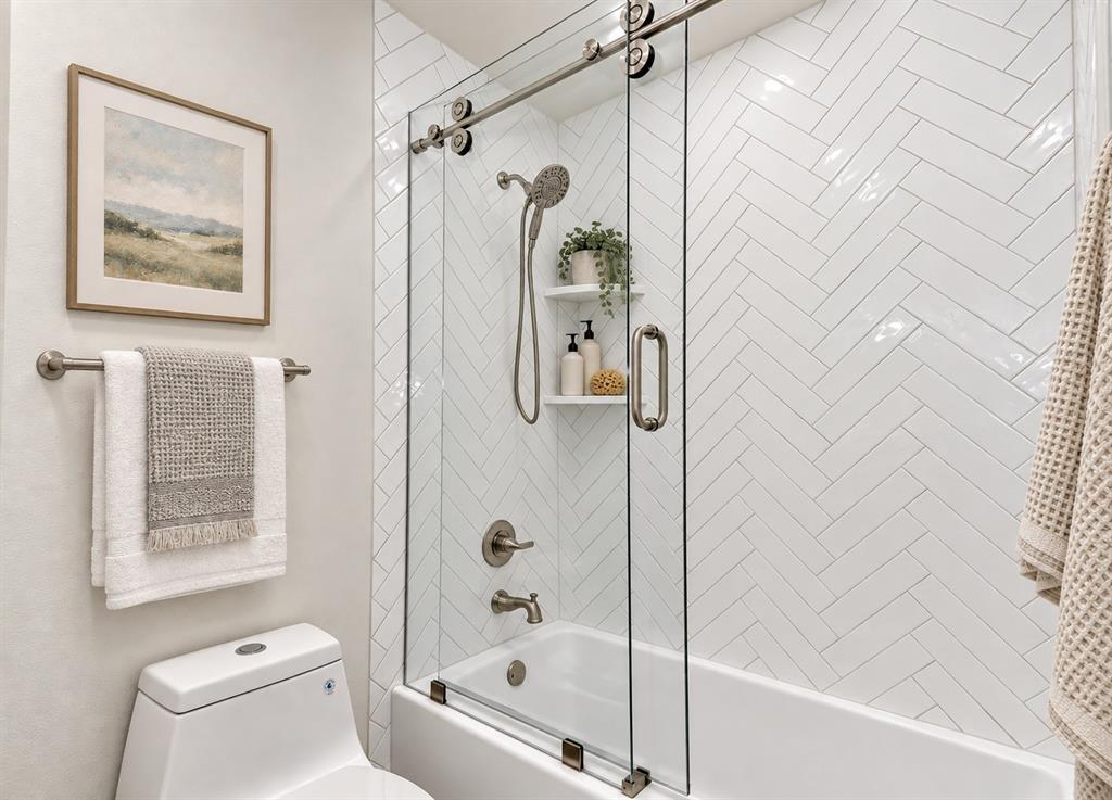 Herringbone tile shower surround, integrated bathtub, sliding glass shower door and a recessed shower shelf