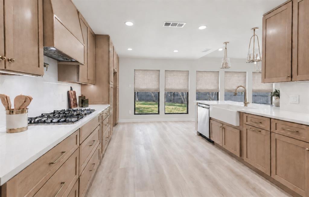 Wood-finish cabinetry with brass hardware, gas range, a farmhouse sink, and recessed lighting