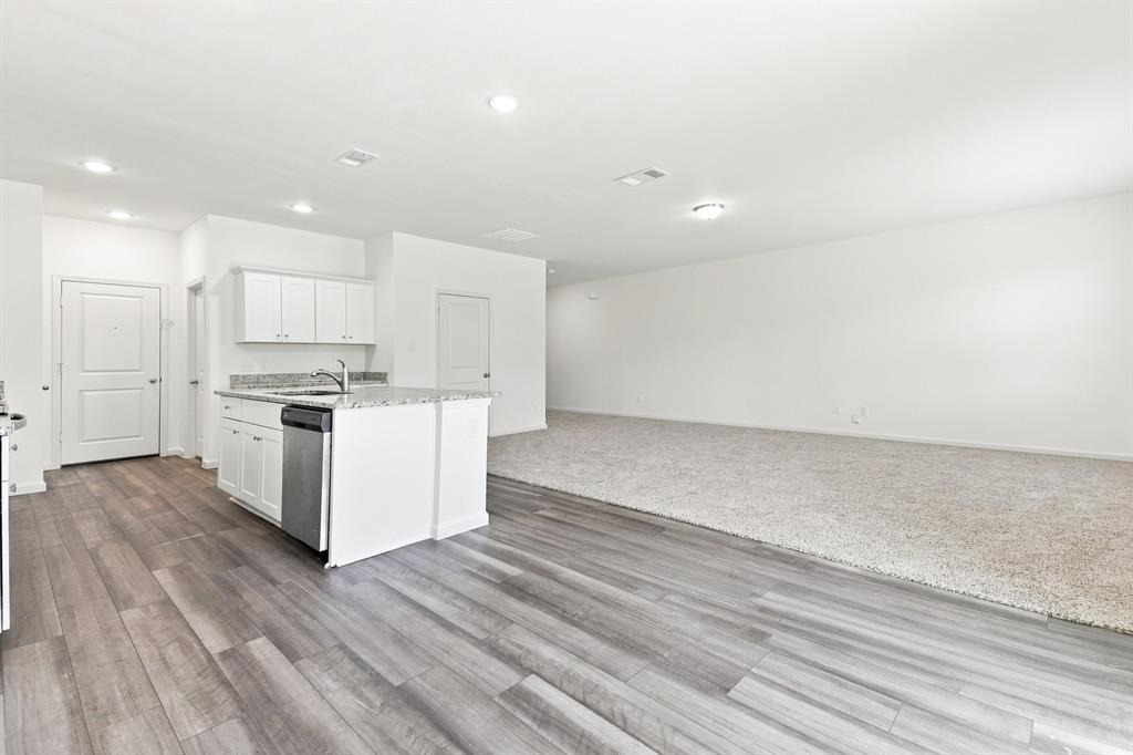 Open-concept living space featuring wood-finish flooring, white cabinetry, a kitchen island with a built-in sink and dishwasher, recessed lighting, and light-colored carpeting Open-concept living space featuring wood-finish flooring, white cabinetry, a kitchen island with a built-in sink and dishwasher, recessed lighting, and light-colored carpeting