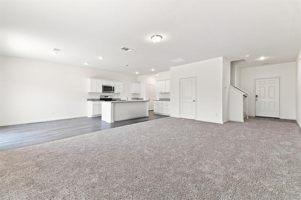 Spacious living area featuring light gray carpeting and a kitchen with white cabinetry, stainless steel microwave, and an island with a countertop Spacious living area featuring light gray carpeting and a kitchen with white cabinetry, stainless steel microwave, and an island with a countertop