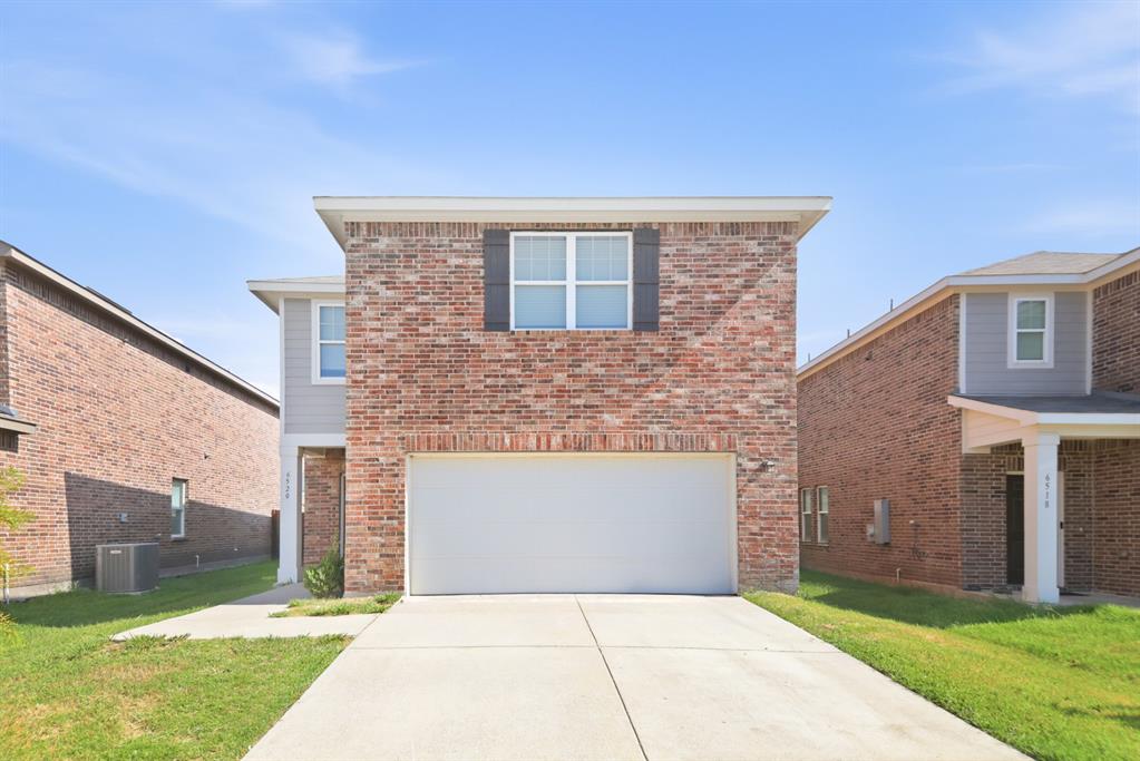Two-story brick facade home featuring an integrated garage, a concrete driveway, and a visible air conditioning unit