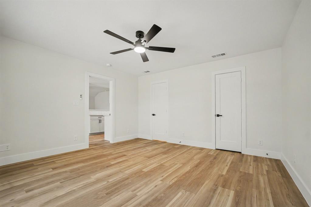 Spacious primary bedroom featuring wood-finish flooring, white walls, and a contemporary ceiling fan