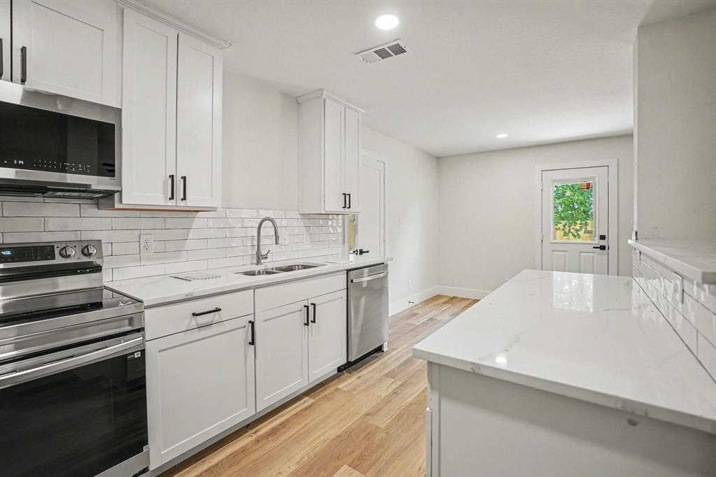 Modern kitchen featuring white shaker cabinetry with black hardware, stainless steel appliances, a subway tile backsplash, and light wood-finish flooring