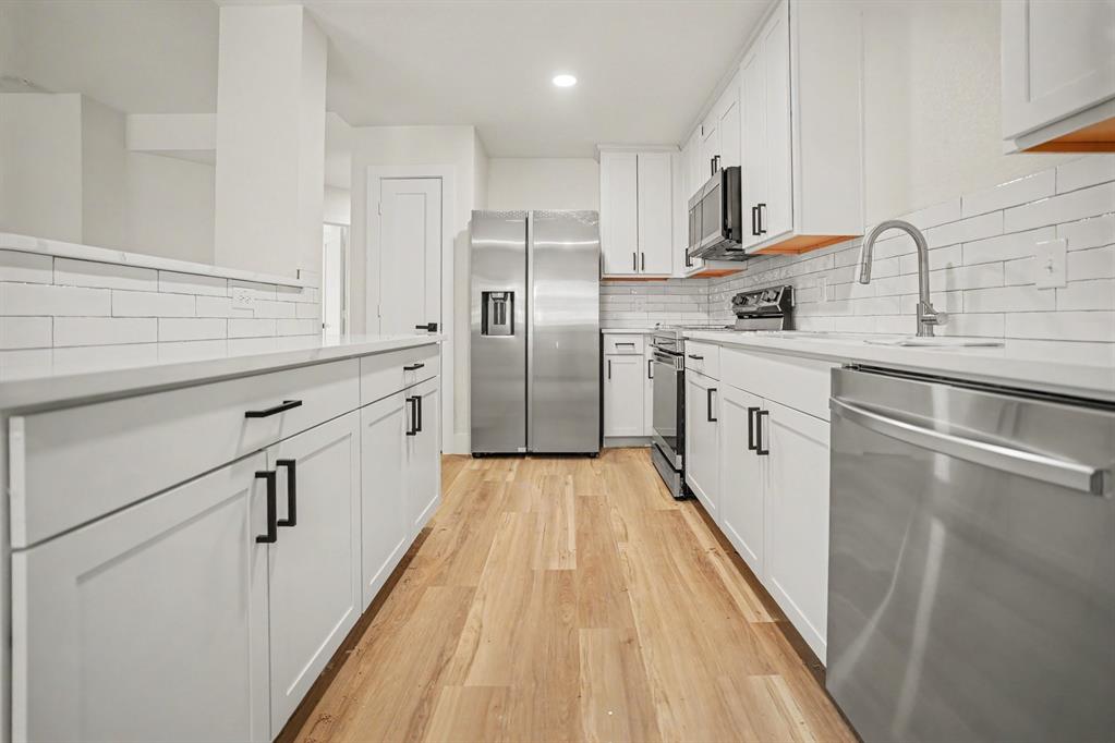 Modern kitchen featuring white shaker cabinetry, stainless steel appliances, light countertops, wood-finish flooring, and subway tile backsplash