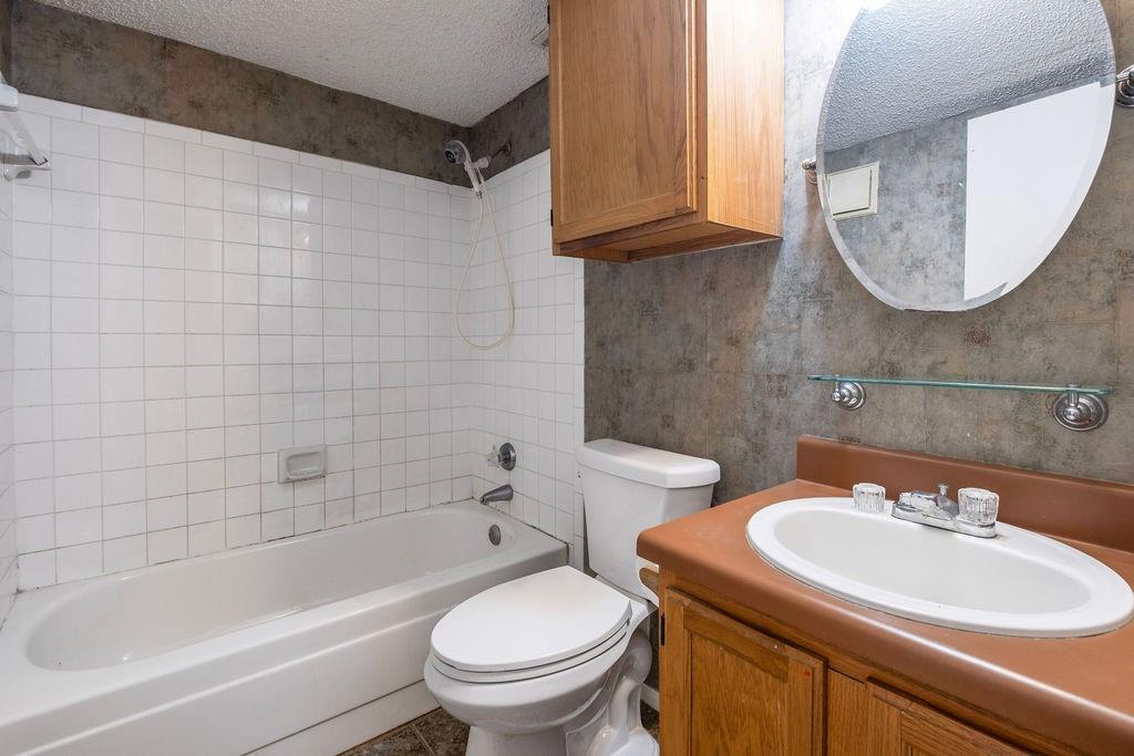 Bathroom featuring a white bathtub with tile surround, a built-in wood-finish vanity with an integrated sink, an oval mirror, and a wall-mounted wood-finish cabinet
