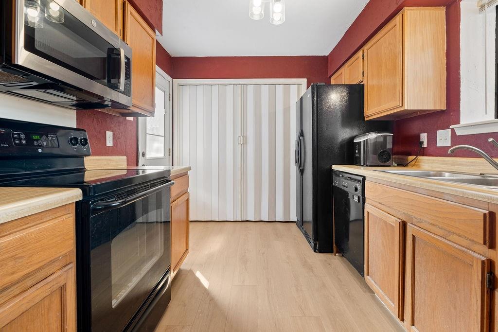 Kitchen featuring wood-finish flooring, wood cabinetry, stainless steel microwave, black electric range, and black dishwasher Kitchen featuring wood-finish flooring, wood cabinetry, stainless steel microwave, black electric range, and black dishwasher