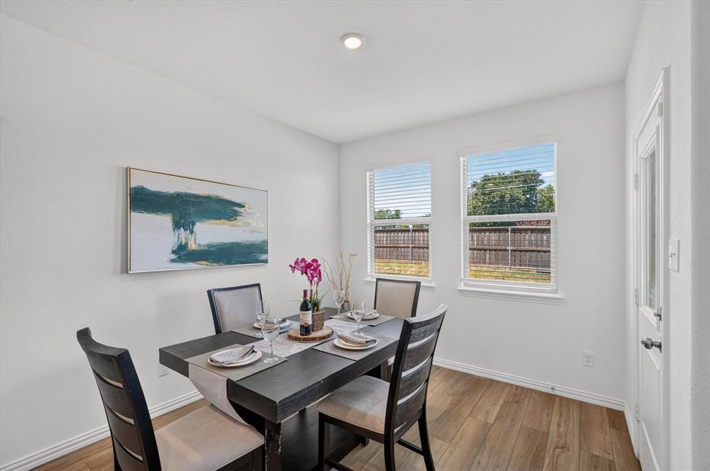 Dedicated dining space featuring a black wood table with seating for four, wood-finish flooring, recessed ceiling lighting, and dual windows with plantation shutters offering natural light and outdoor views