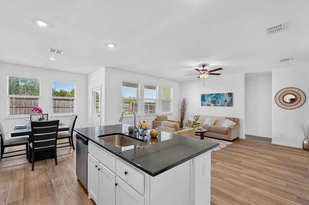 Kitchen island with a stainless steel sink, dark countertop, and white cabinetry