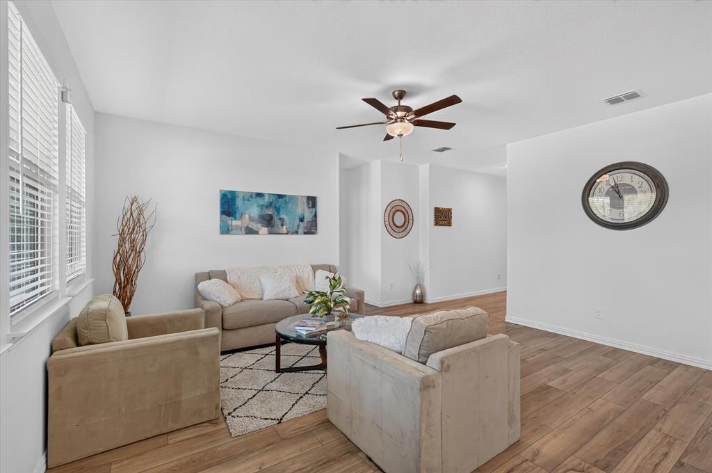 Living area featuring wood-finish flooring, white walls, and a ceiling fan with integrated lighting