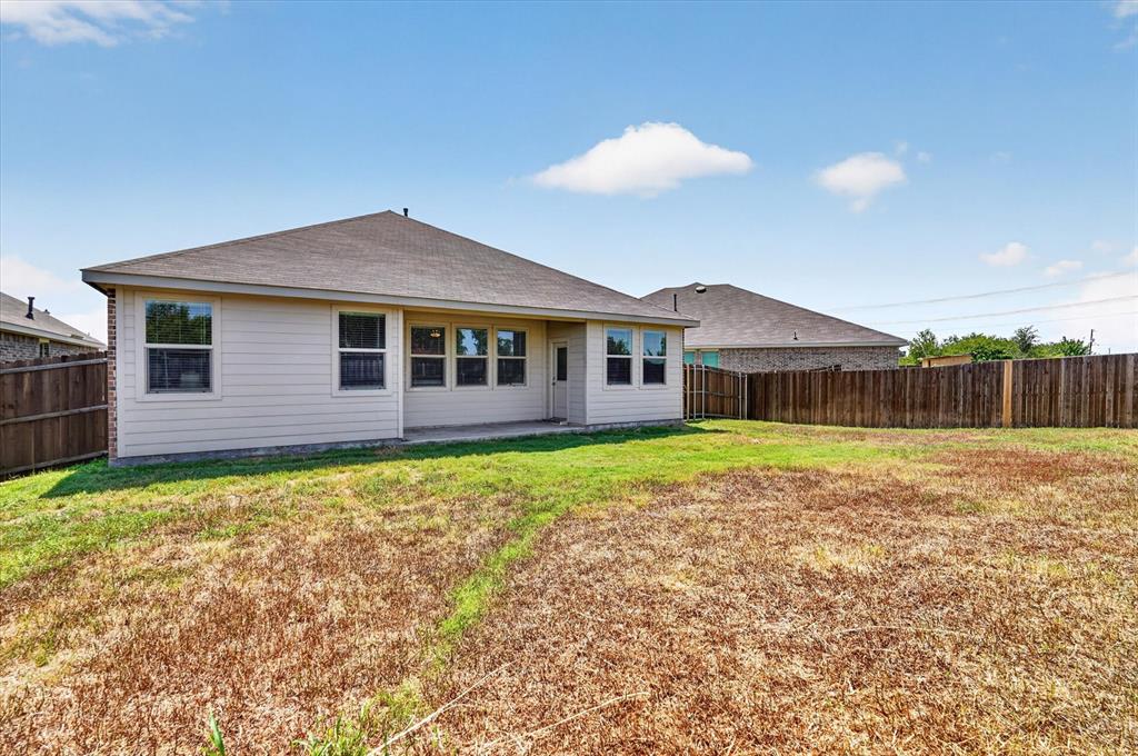 Rear exterior featuring a neutral-toned siding, multiple windows, a concrete patio, and a wood privacy fence