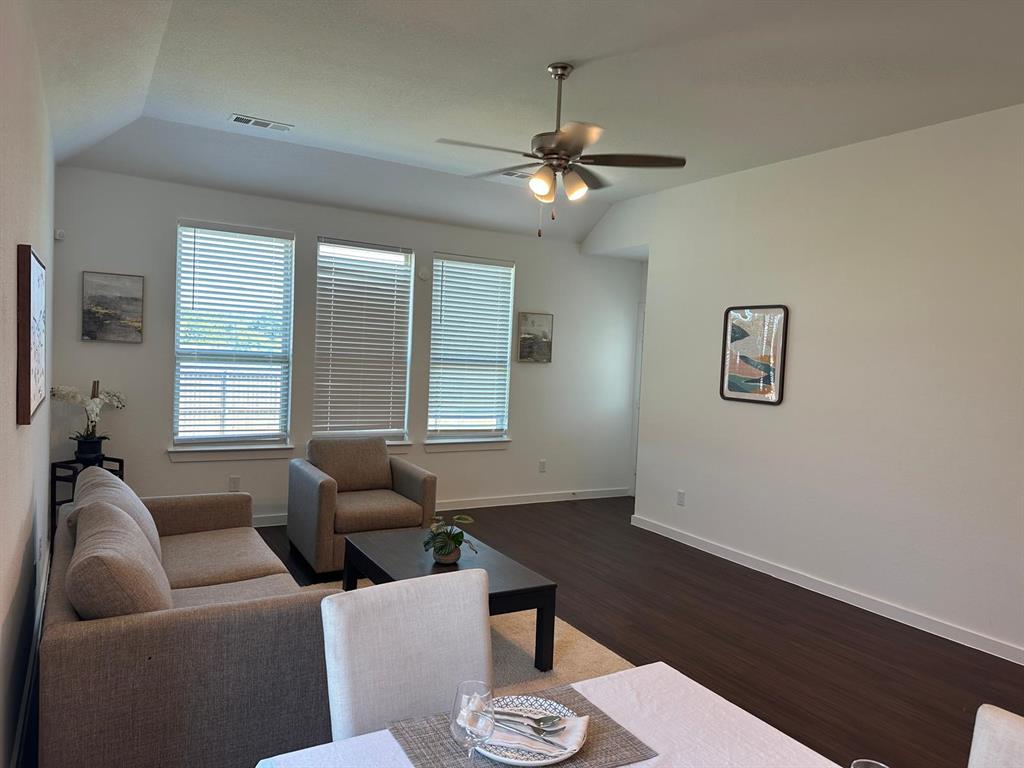 Vaulted ceiling with a ceiling fan, three windows with blinds, and wood-finish flooring