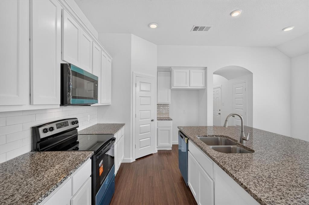 Galley-style kitchen featuring white cabinetry, granite countertops, stainless steel appliances including a gas range and microwave, dual undermount sinks with gooseneck faucet, and wood-finish flooring throughout