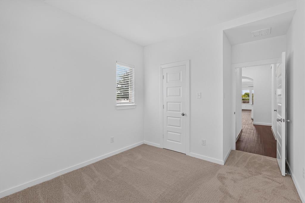Bright bedroom featuring neutral carpeting, white six-panel interior doors, and a small fixed window with plantation shutters