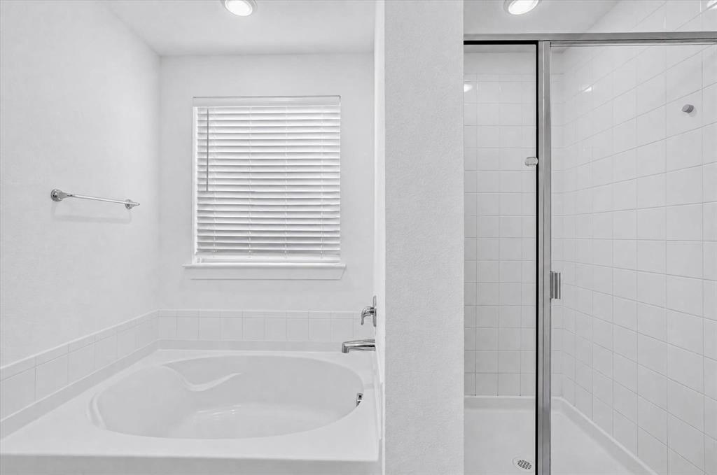 Spa-inspired primary bathroom featuring a deep soaking tub with integrated armrests, white subway tile surround, recessed ceiling lighting, and a frameless glass-enclosed shower stall with chrome hardware
