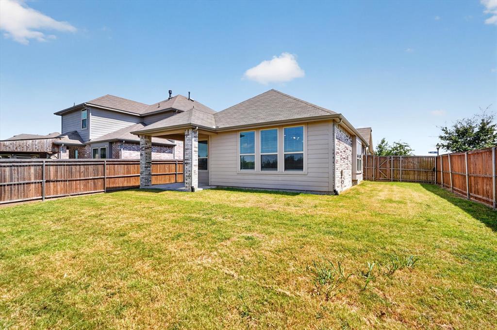 Expansive backyard featuring a covered patio with stone columns, a wood privacy fence, and multiple windows across the rear elevation