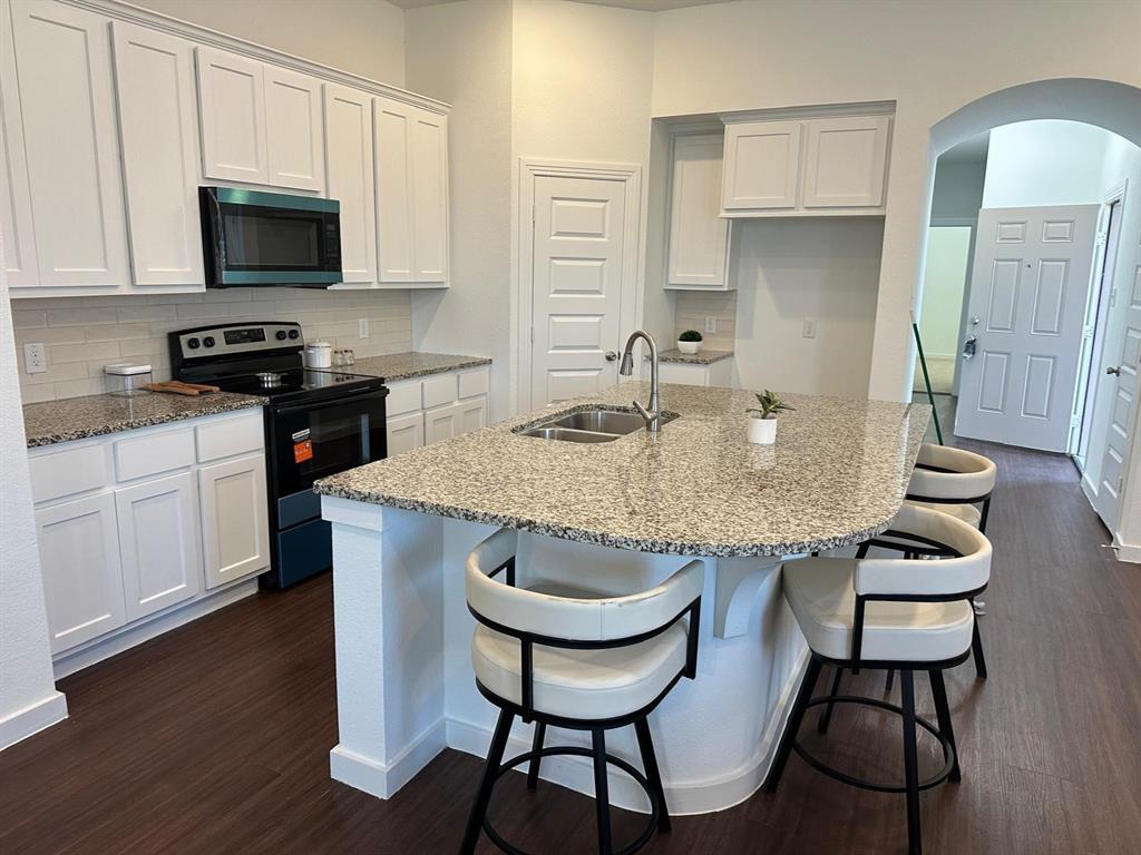 Kitchen featuring an island with an undermount double basin sink, granite countertops, white cabinetry, a subway tile backsplash, and wood-finish flooring