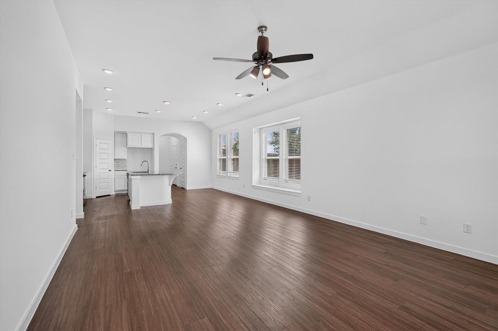 Spacious open-concept living area featuring rich wood-finish flooring throughout, white walls, and abundant natural light from multiple glass doors and windows