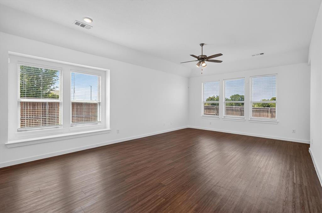Spacious room featuring gleaming wood-finish flooring, abundant natural light from dual window banks, ceiling fan with integrated lighting, and clean white walls with neutral trim throughout