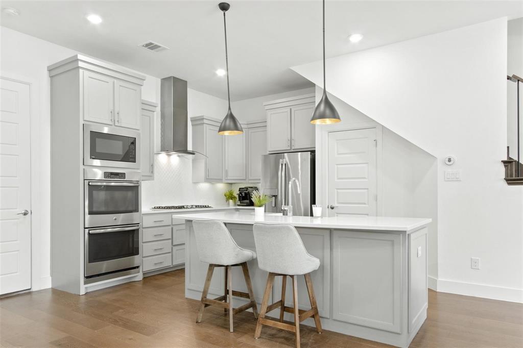 Open-concept kitchen featuring an island with seating, stainless steel appliances, light gray cabinetry, and wood-finish flooring