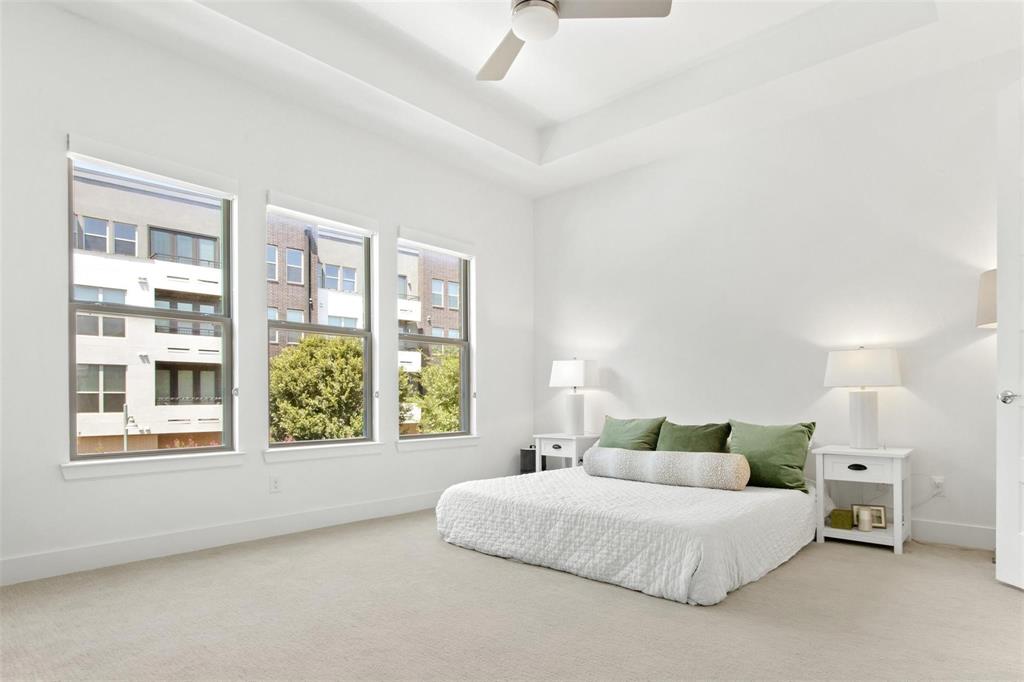 Bright room featuring three large windows, a tray ceiling, recessed lighting, a ceiling fan, and light-toned carpeting
