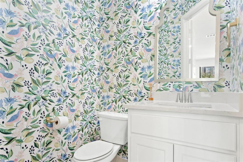 Powder room featuring botanical and bird-patterned wallpaper, white vanity with paneled cabinetry, integrated sink, and chrome faucet