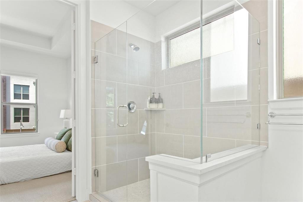 Frameless glass shower enclosure featuring large format light gray wall tiles and a built-in shower niche