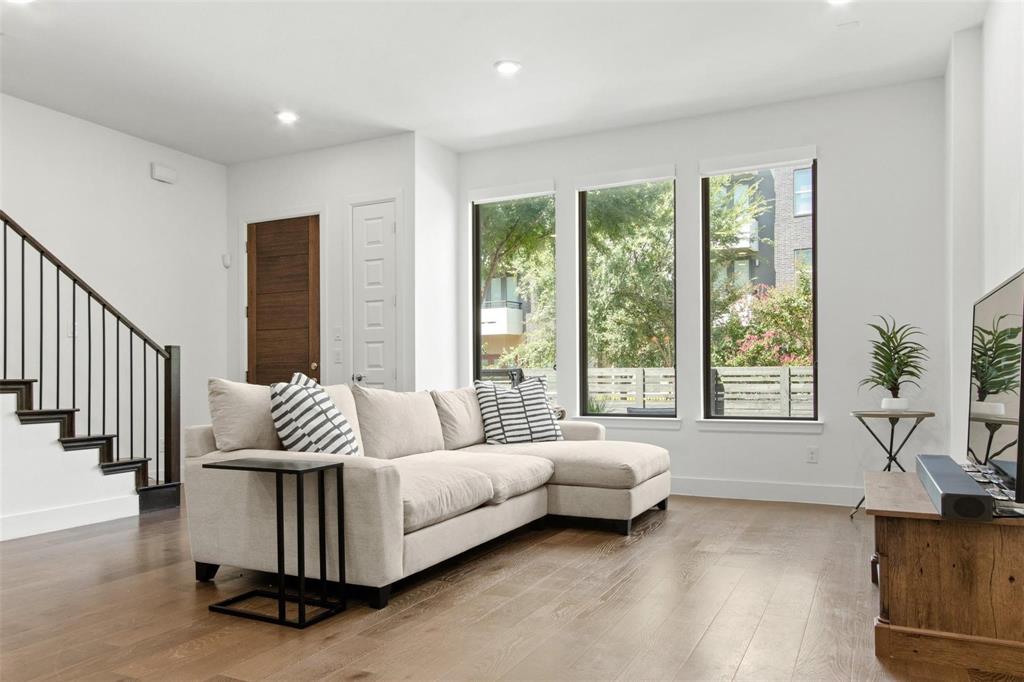 Living area featuring three large windows, recessed lighting, wood-finish flooring, and a dark wood staircase with black metal balusters