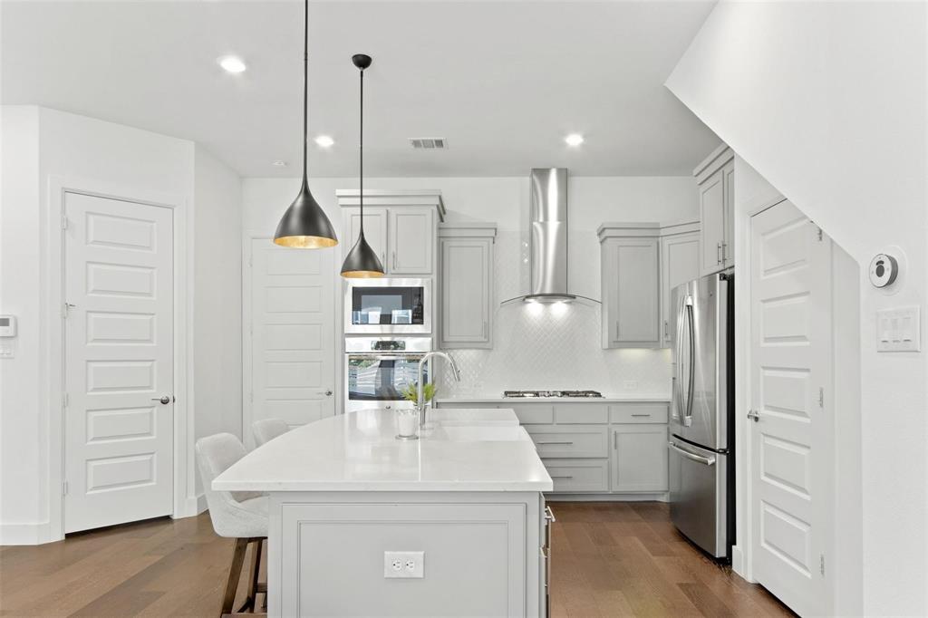 Contemporary kitchen featuring a large central island with seating, stainless steel appliances, light gray cabinetry, and a white subway tile backsplash