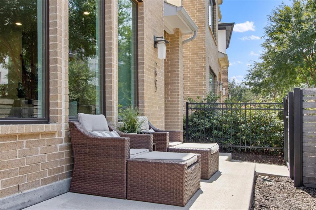 Brick exterior with multiple tall windows, featuring a concrete patio, black metal fencing, and a modern slatted gate
