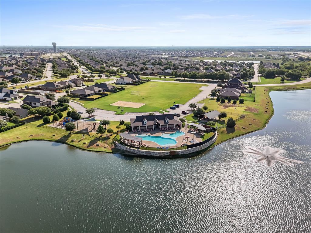 Community lakefront amenity center featuring a swimming pool with integrated spa, a shaded outdoor lounge area, and an adjacent playground