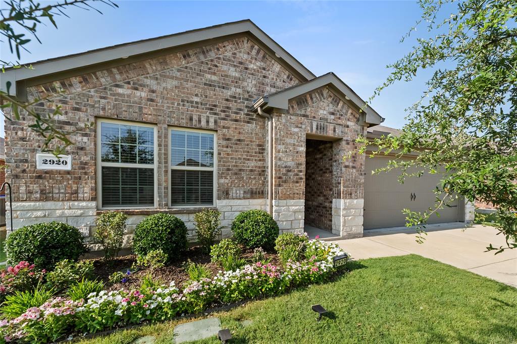 Brick and stone facade residence featuring a covered entry, an attached garage, and a landscaped front yard with decorative plantings
