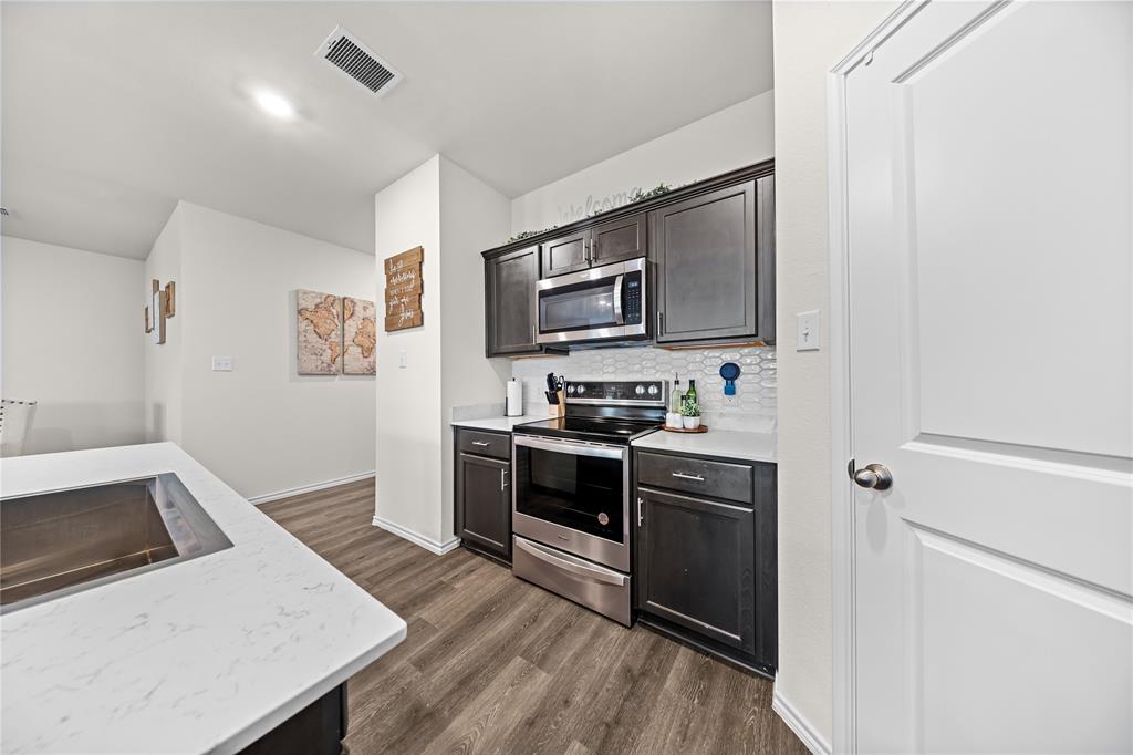 Kitchen featuring dark wood-finish cabinetry, stainless steel appliances including a microwave and range, light-toned countertops, and a white hexagonal tile backsplash