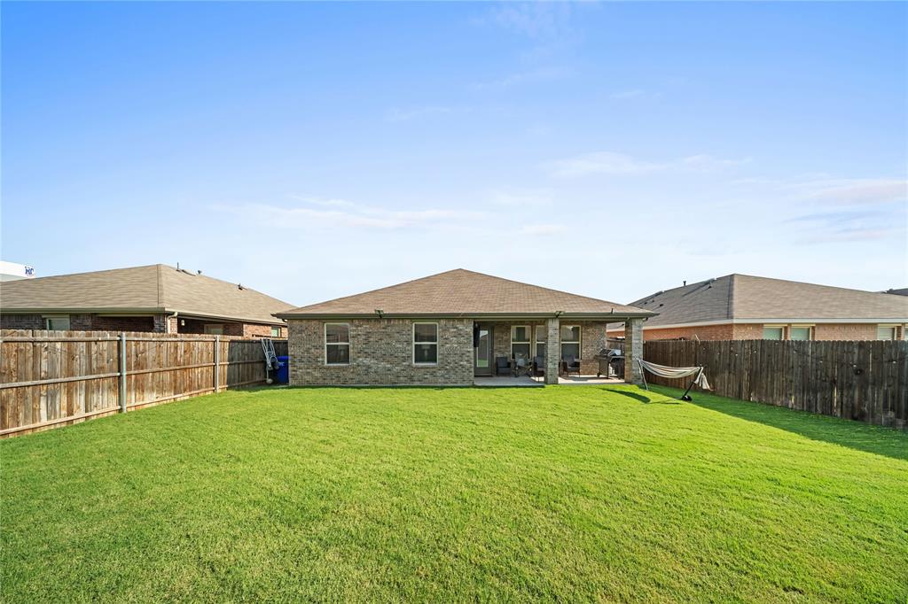 Expansive backyard featuring a manicured lawn, full privacy fencing, and a covered concrete patio