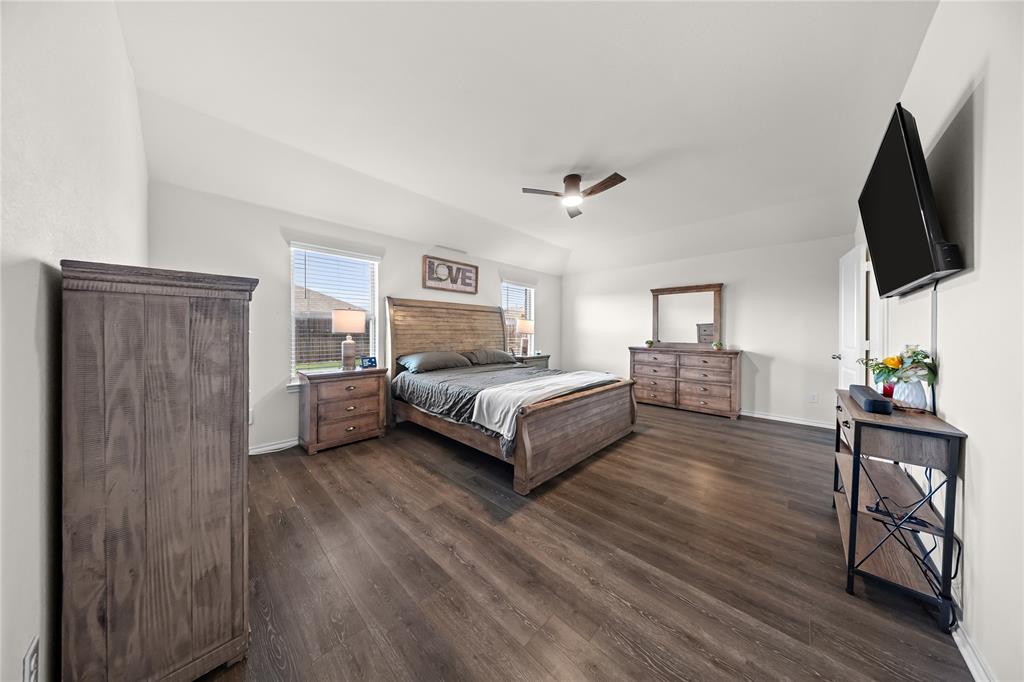 Spacious room featuring wood-finish flooring, two windows with blinds, a ceiling fan, and white walls