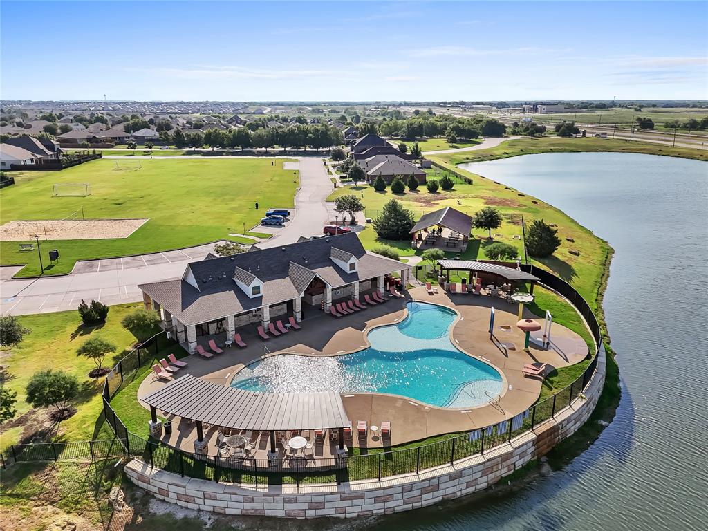 Community clubhouse with a large swimming pool, surrounded by a lake, expansive green space, and a sand volleyball court