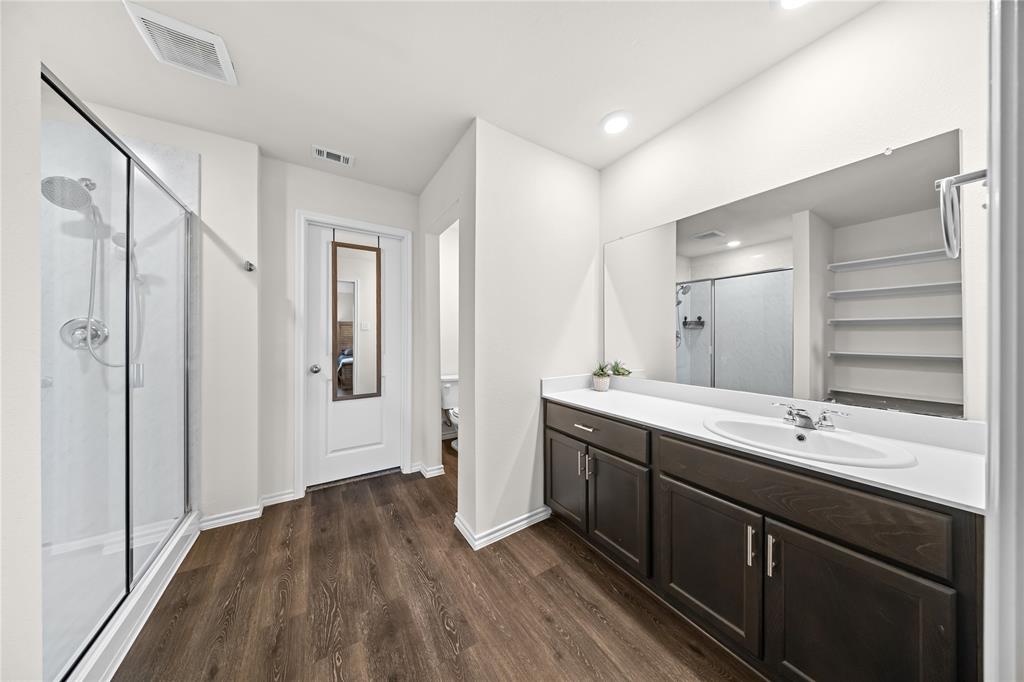 Spacious bathroom featuring a glass-enclosed shower, expansive vanity with a single basin sink, rich wood-finish cabinetry, and wood-finish flooring