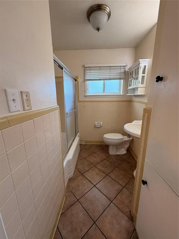 Bathroom featuring tile flooring, a tub-shower combination with a sliding glass door, a wall-mounted medicine cabinet, and a pedestal sink