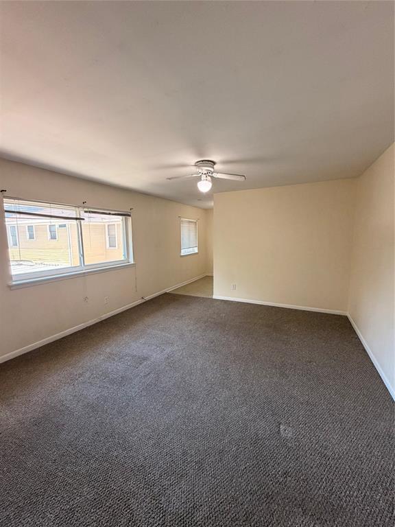 Interior space featuring neutral wall tones, wall-to-wall carpeting, multiple windows with horizontal blinds, and a central ceiling fan with an integrated light fixture