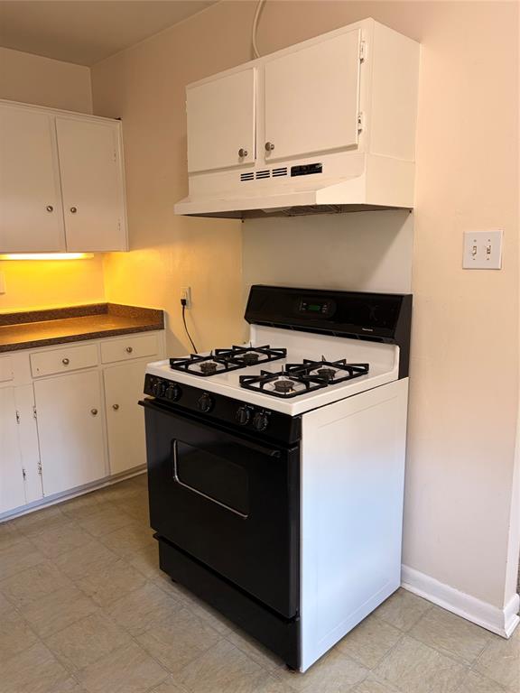 White cabinetry, solid-surface countertops, and a black-and-white gas range with an integrated hood